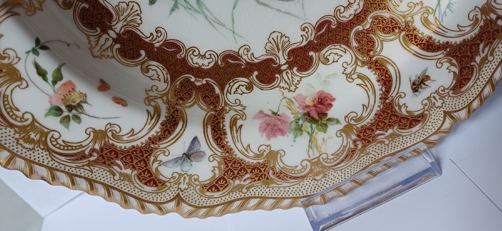 A circular late-Victorian Royal Worcester porcelain soup dish featuring hand-painted botanical floral and insect motifs enclosed within elaborate red and gold gilded rococo scroll borders. View XII