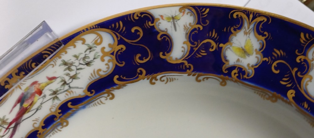 An antique circular porcelain soup dish featuring a dark cobalt blue rim with ornate gold scrollwork, painted birds, and butterflies in the centre. View X