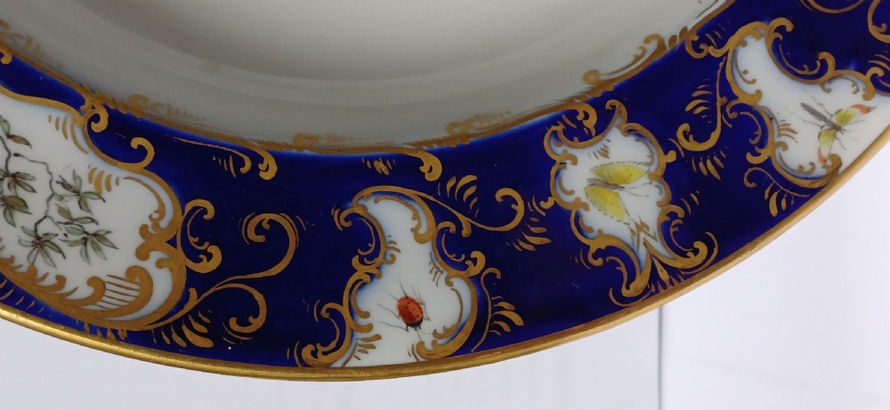 An antique circular porcelain soup dish featuring a dark cobalt blue rim with ornate gold scrollwork, painted birds, and butterflies in the centre. View XI