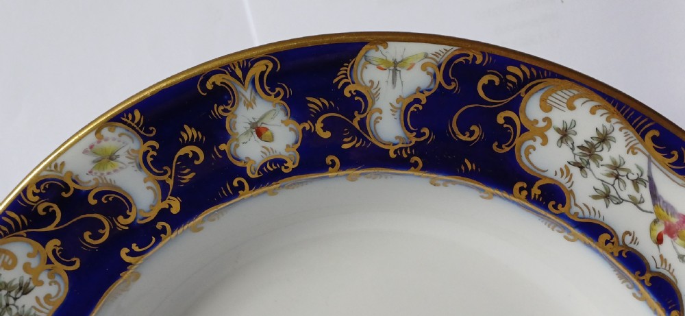An antique circular porcelain soup dish featuring a dark cobalt blue rim with ornate gold scrollwork, painted birds, and butterflies in the centre. View XIII