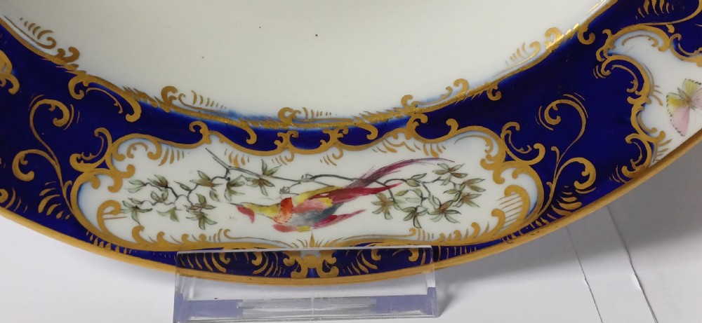 An antique circular porcelain soup dish featuring a dark cobalt blue rim with ornate gold scrollwork, painted birds, and butterflies in the centre. View XV