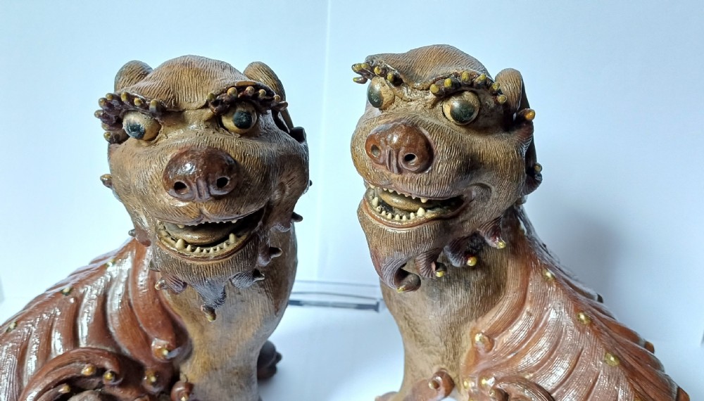 A pair of antique brown glazed ceramic Chinese Shiwan Buddhistic lion dogs depicted sitting upright with open mouths and detailed carved fur. View X