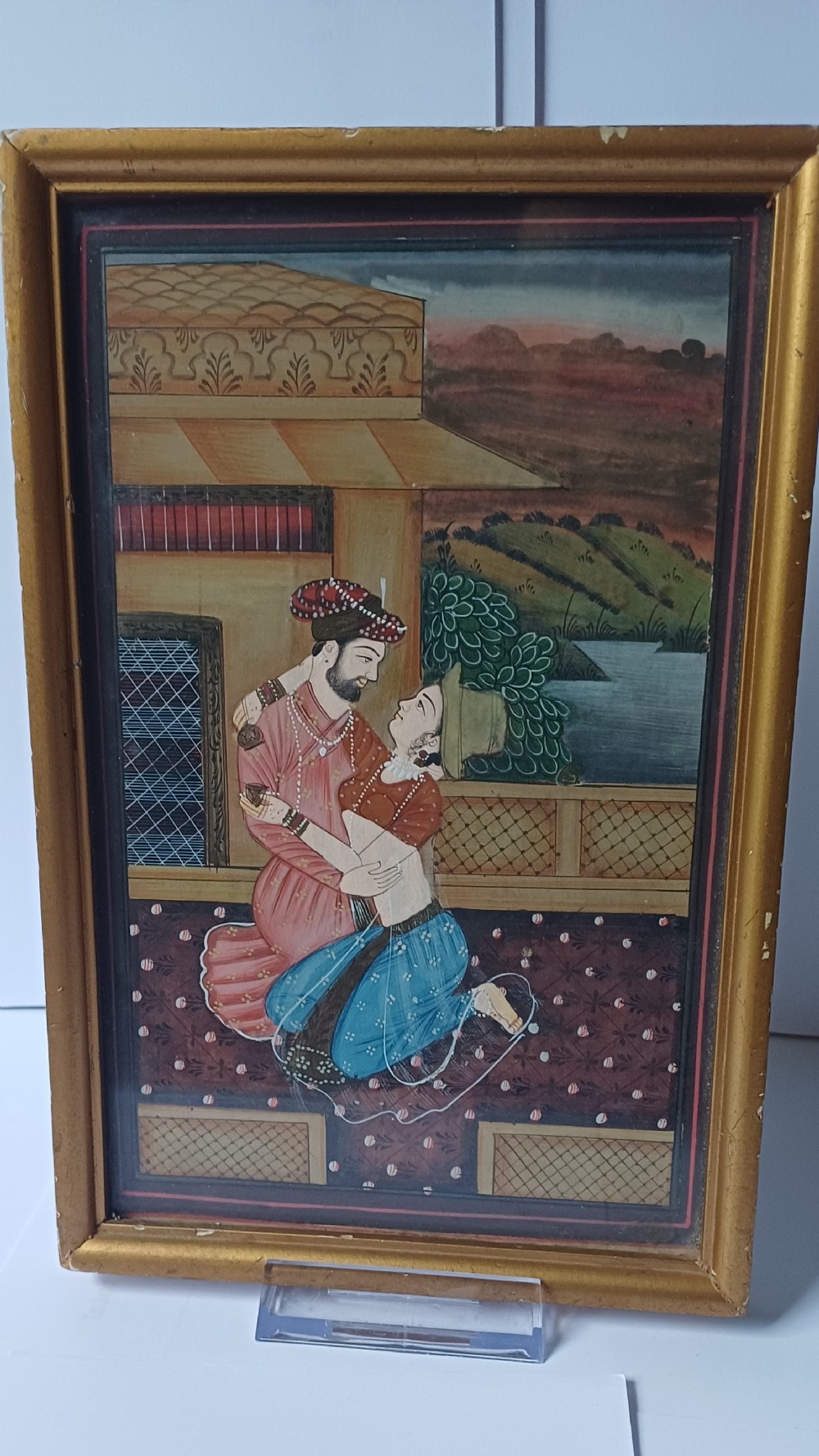 A late 19th-century framed Indian gouache miniature painting depicting a royal couple embracing on a terrace, set within a gilt wood frame.