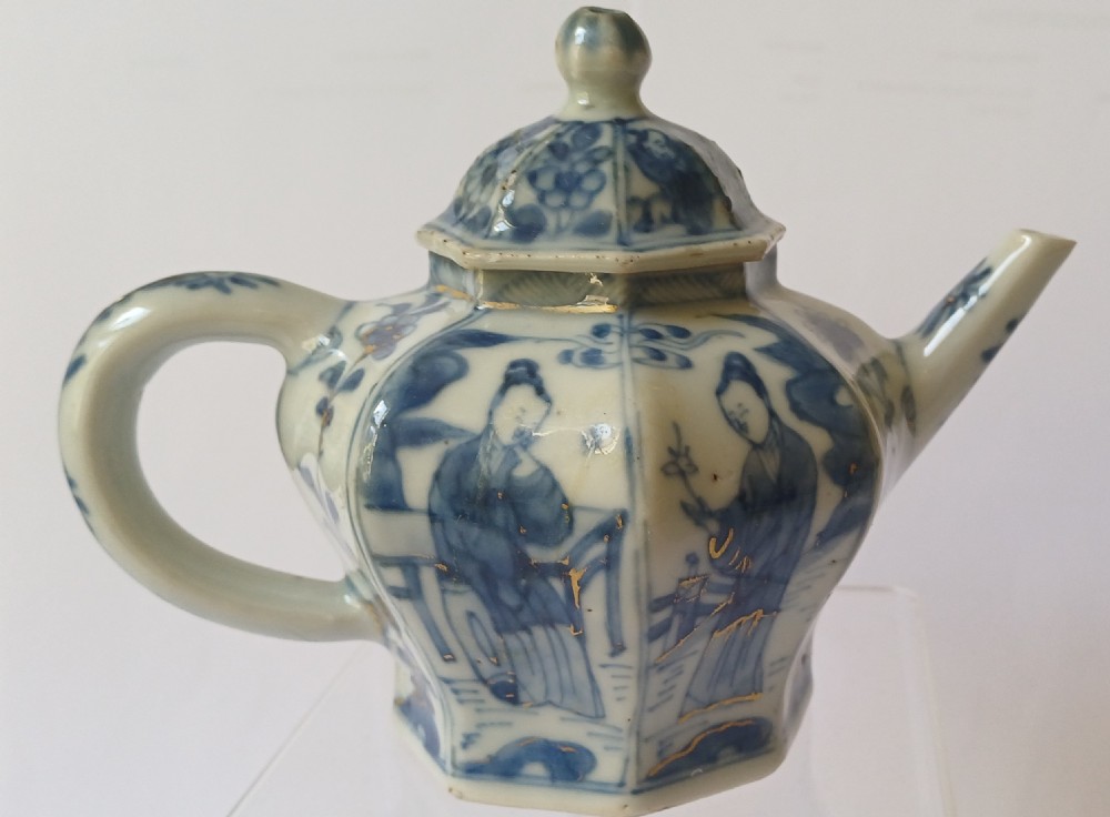 An octagonal Chinese porcelain teapot decorated with cobalt blue figures in landscapes and gold leaf highlights.