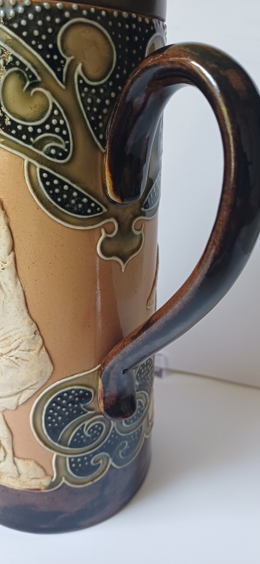 An Art Nouveau Doulton Lambeth glazed stoneware jug featuring relief figures of sports players alongside dark brown glazes and stylised swirl patterns. View XVIII