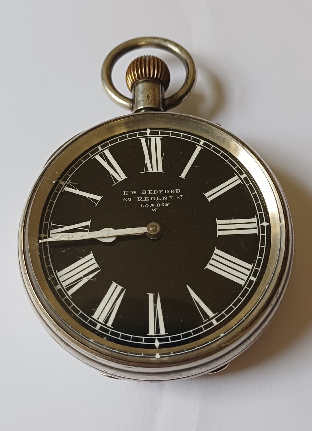 An oversized Edwardian silver-cased pocket watch featuring a black dial with white Roman numerals and a brass winding crown. View III