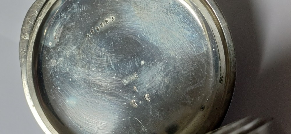 An oversized Edwardian silver-cased pocket watch featuring a black dial with white Roman numerals and a brass winding crown. View VI