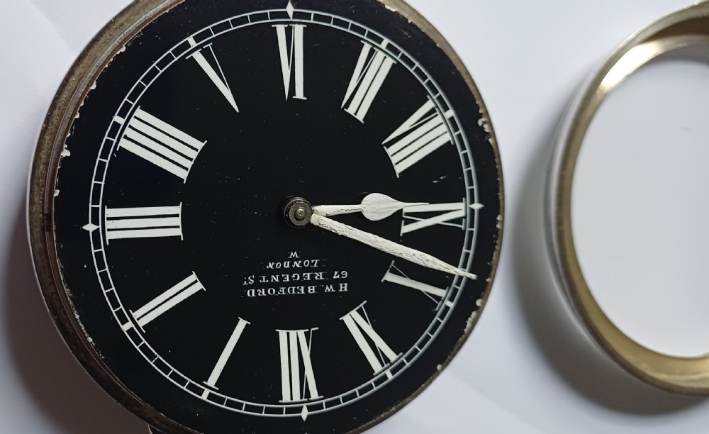 An oversized Edwardian silver-cased pocket watch featuring a black dial with white Roman numerals and a brass winding crown. View XII
