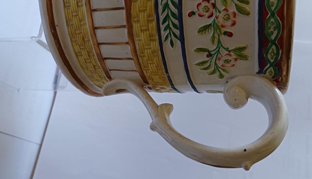 A Georgian pearlware ceramic mug featuring polychrome relief-moulded floral garlands, basketweave bands, gilt accents, and the word WARRANTED. View III