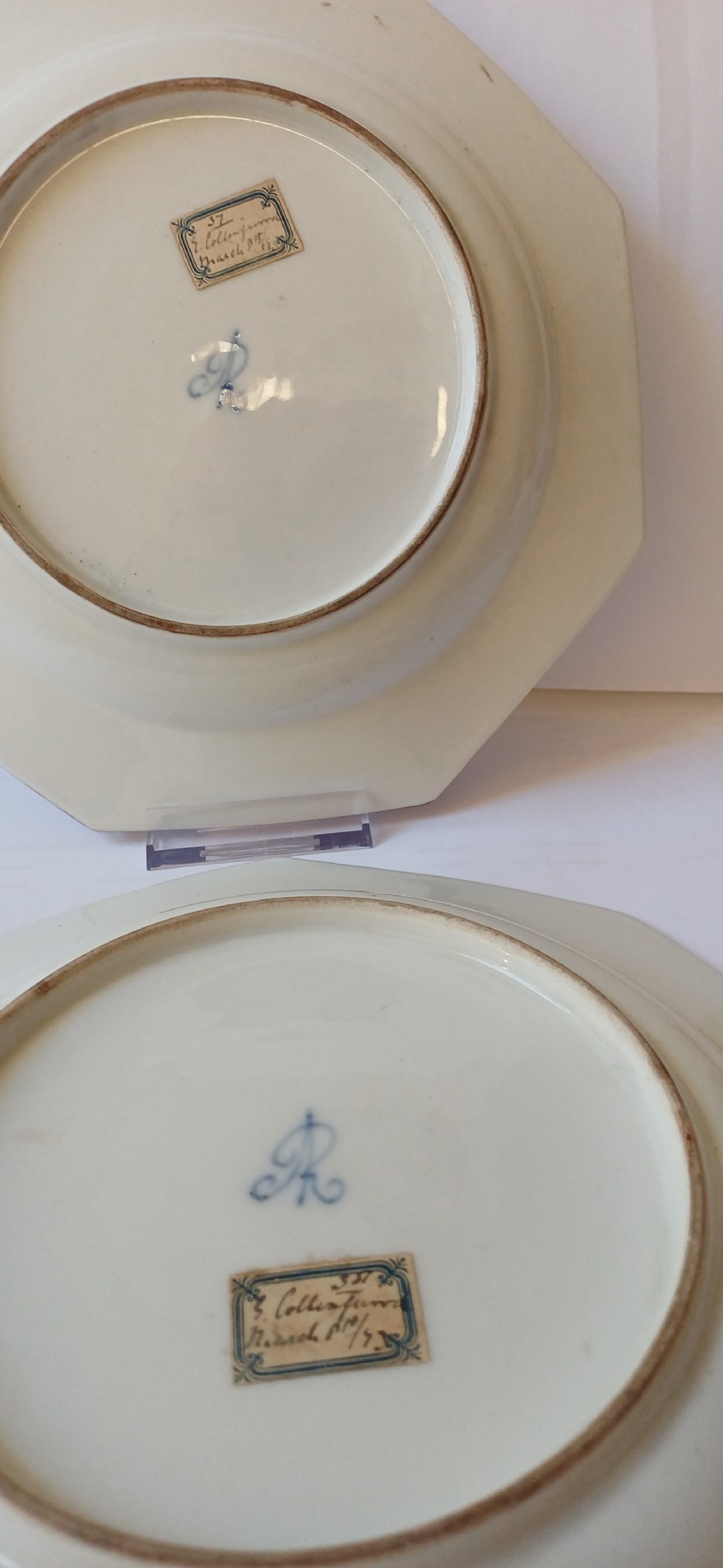 A pair of octagonal white porcelain cabinet plates featuring hand-painted romantic pastoral scenes in the centre, framed by elaborate gilt scrollwork, floral motifs, and decorative rim cartouches. View V