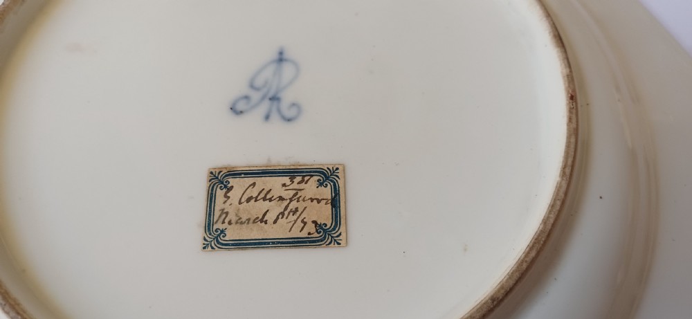 A pair of octagonal white porcelain cabinet plates featuring hand-painted romantic pastoral scenes in the centre, framed by elaborate gilt scrollwork, floral motifs, and decorative rim cartouches. View VI