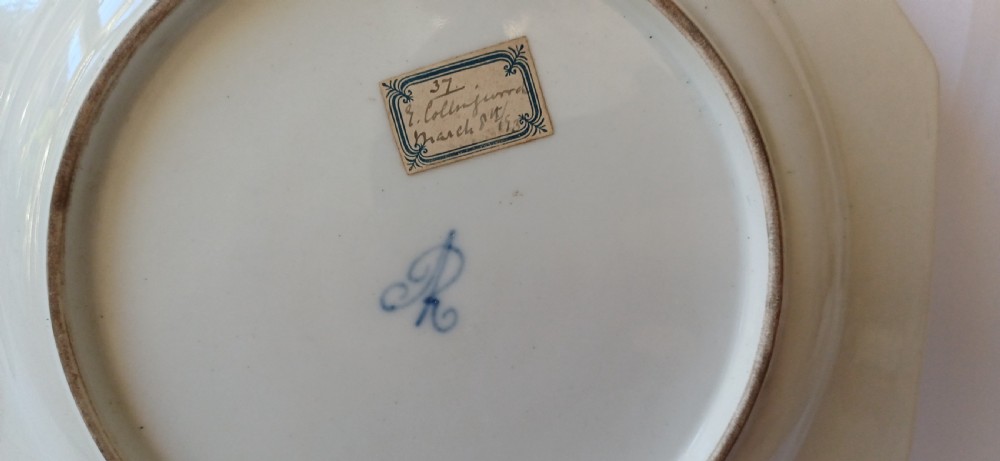 A pair of octagonal white porcelain cabinet plates featuring hand-painted romantic pastoral scenes in the centre, framed by elaborate gilt scrollwork, floral motifs, and decorative rim cartouches. View VII