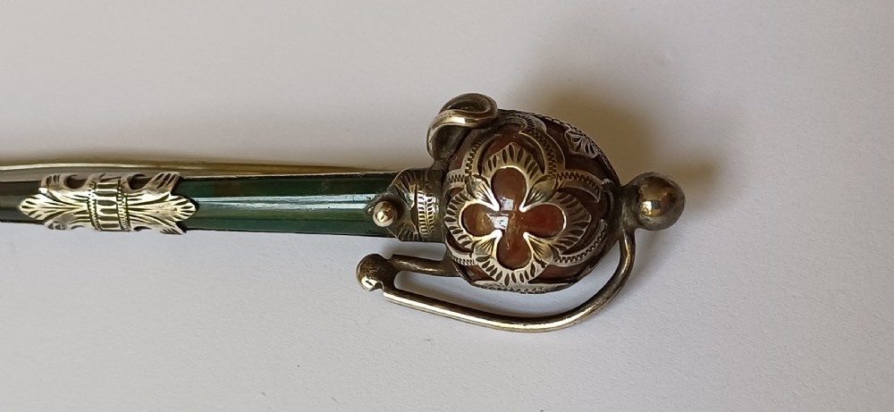 An antique silver kilt pin crafted in the shape of a Scottish basket-hilted broadsword inlaid with green and brown polished agate stones. View II