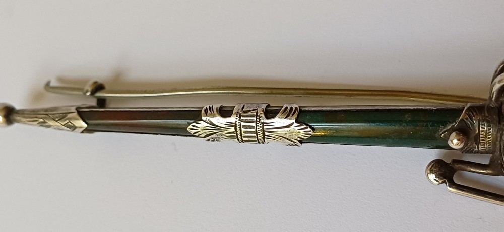 An antique silver kilt pin crafted in the shape of a Scottish basket-hilted broadsword inlaid with green and brown polished agate stones. View IX