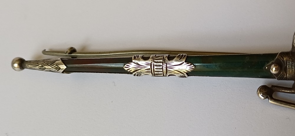 An antique silver kilt pin crafted in the shape of a Scottish basket-hilted broadsword inlaid with green and brown polished agate stones. View X