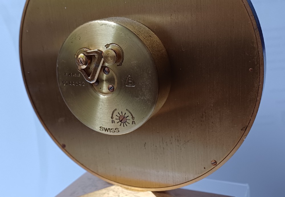 A mid-century Imhof gilt brass desk clock featuring a round textured gold dial with Roman numerals and a faceted rectangular pedestal base. View VII