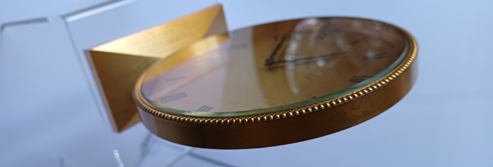 A mid-century Imhof gilt brass desk clock featuring a round textured gold dial with Roman numerals and a faceted rectangular pedestal base. View XII