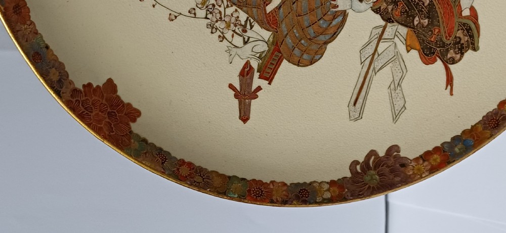 A circular shallow cream earthenware dish featuring hand-painted figures in traditional clothing framed by a gilded floral border. View VII