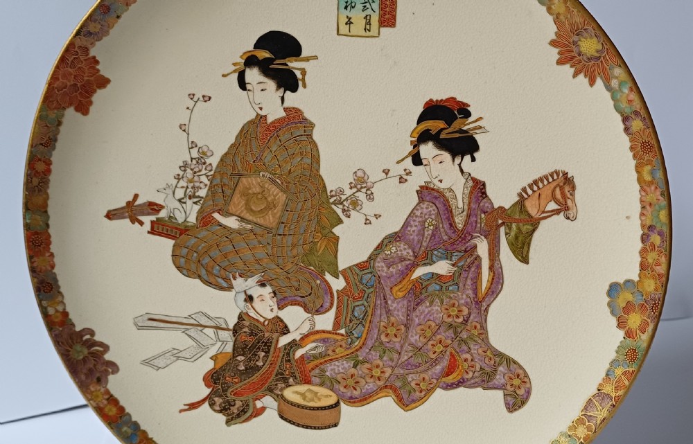 A circular shallow cream earthenware dish featuring hand-painted figures in traditional clothing framed by a gilded floral border. View IX