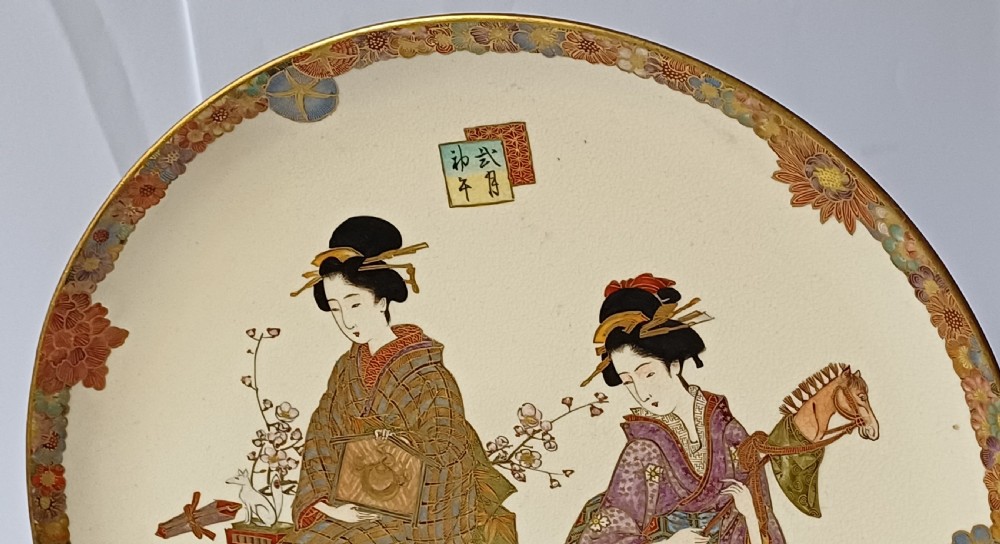 A circular shallow cream earthenware dish featuring hand-painted figures in traditional clothing framed by a gilded floral border. View XXI