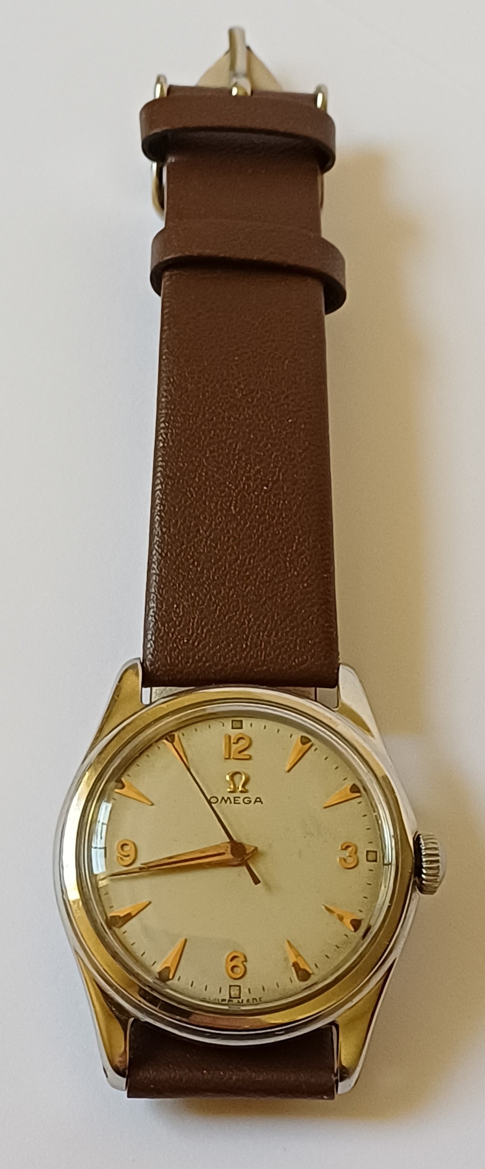 A vintage 1950s Omega wristwatch with a cream dial, gold hour markers, stainless steel case, and a smooth brown leather strap.