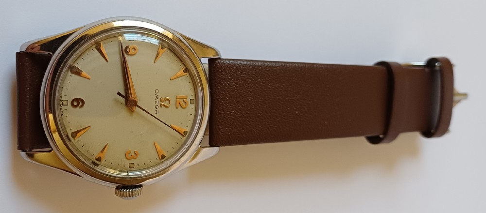 A vintage 1950s Omega wristwatch with a cream dial, gold hour markers, stainless steel case, and a smooth brown leather strap. View II