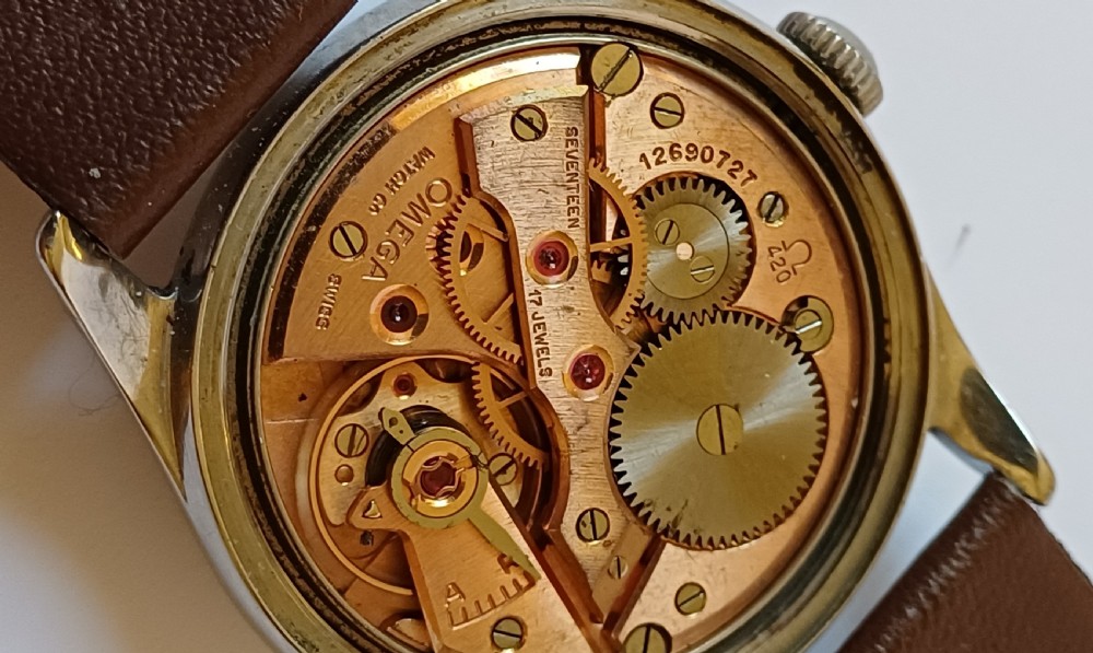 A vintage 1950s Omega wristwatch with a cream dial, gold hour markers, stainless steel case, and a smooth brown leather strap. View X