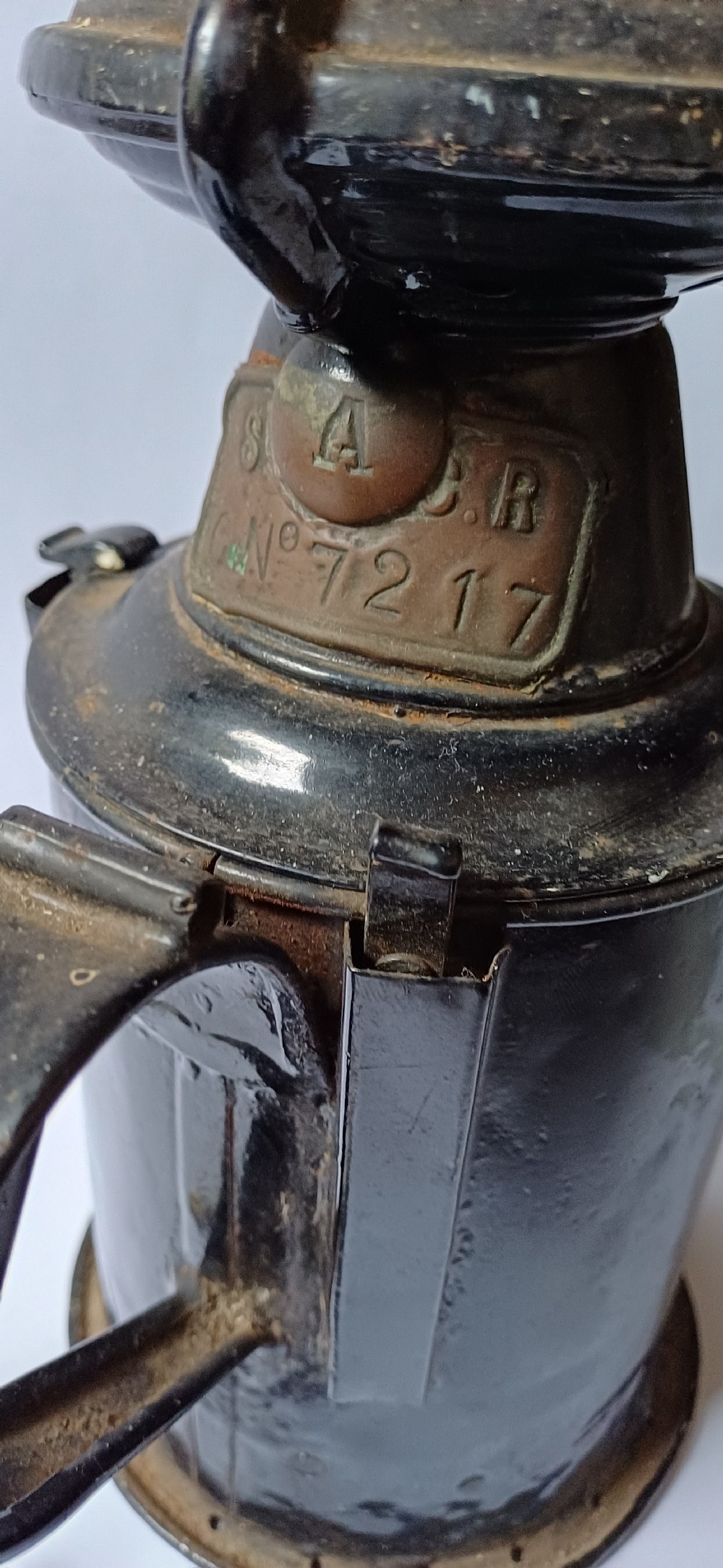 A black painted metal railway lantern with a top carrying handle alongside a silver-coloured pocket watch displaying Roman numerals. View VII