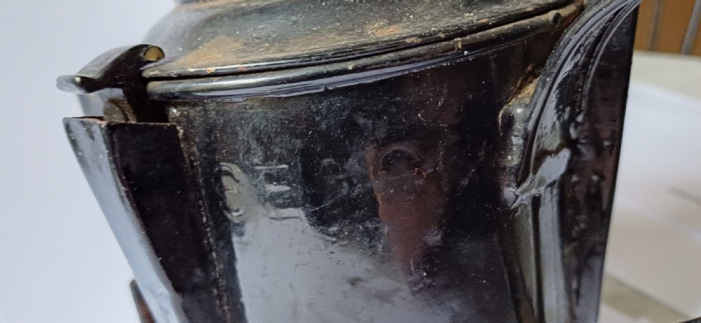 A black painted metal railway lantern with a top carrying handle alongside a silver-coloured pocket watch displaying Roman numerals. View IX