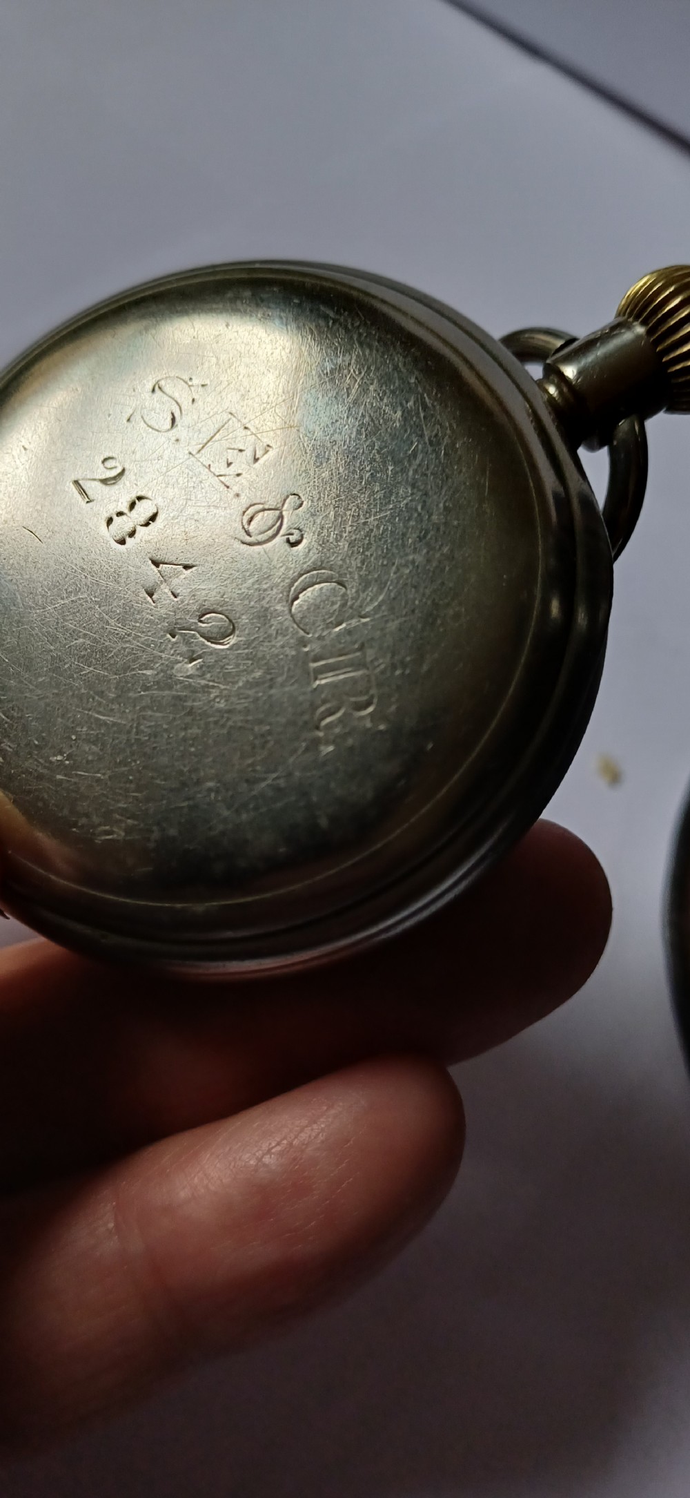 A black painted metal railway lantern with a top carrying handle alongside a silver-coloured pocket watch displaying Roman numerals. View XI