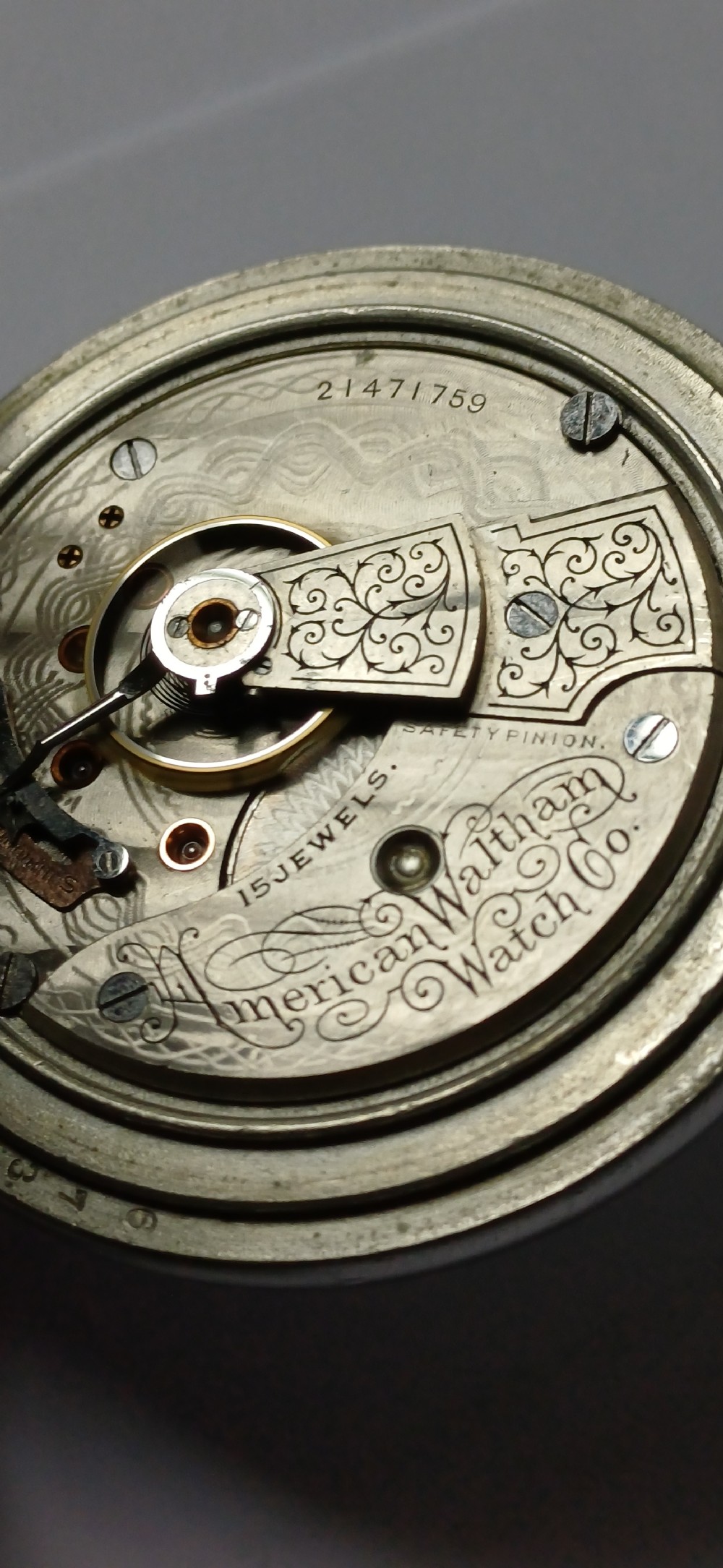 A black painted metal railway lantern with a top carrying handle alongside a silver-coloured pocket watch displaying Roman numerals. View XVII