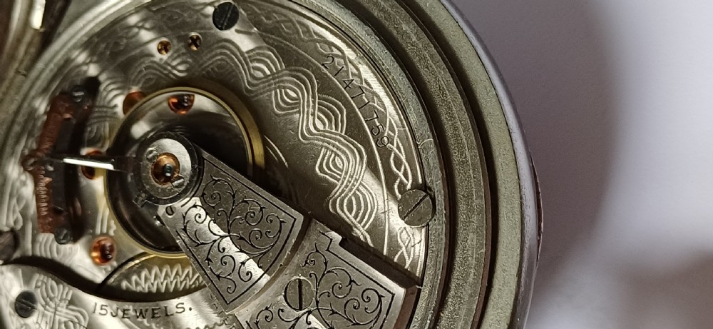 A black painted metal railway lantern with a top carrying handle alongside a silver-coloured pocket watch displaying Roman numerals. View XIX