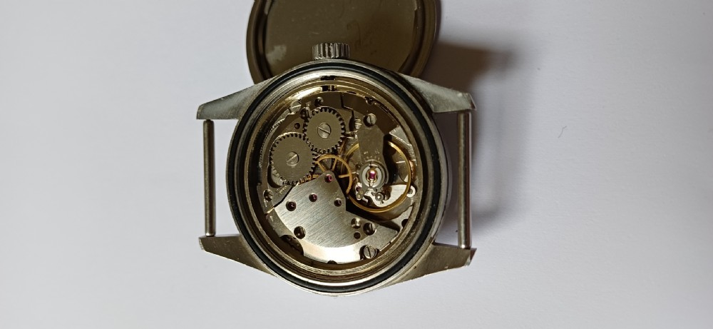 A vintage mid-century military wristwatch featuring a round steel case, a black dial with luminous Arabic numerals, outer minute markings, and luminescent hands. View XI