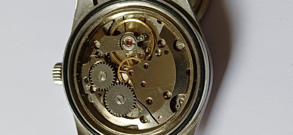 A vintage mid-century military wristwatch featuring a round steel case, a black dial with luminous Arabic numerals, outer minute markings, and luminescent hands. View XIII