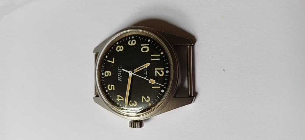 A vintage mid-century military wristwatch featuring a round steel case, a black dial with luminous Arabic numerals, outer minute markings, and luminescent hands. View XV