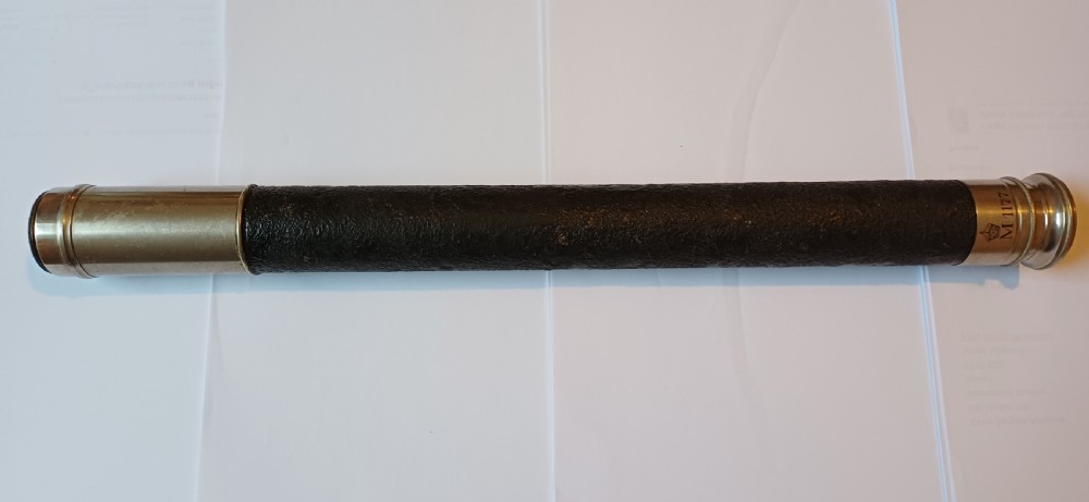 An antique brass single-draw naval telescope wrapped in textured black leather with official markings engraved near the eyepiece.