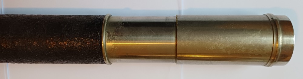 An antique brass single-draw naval telescope wrapped in textured black leather with official markings engraved near the eyepiece. View VIII