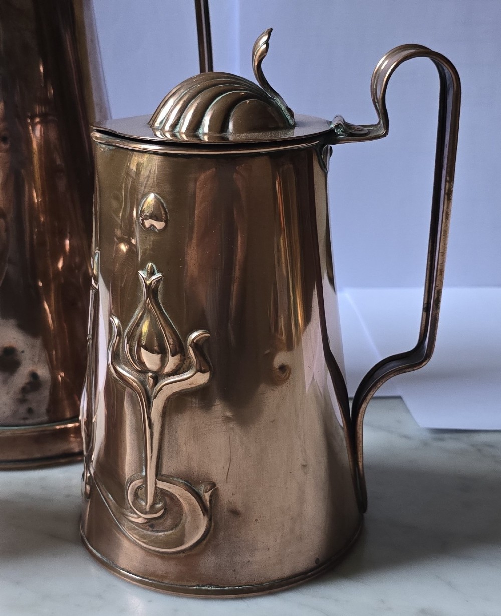 A set of three graduated copper jugs featuring embossed Art Nouveau floral motifs and shell-shaped hinged lids. View III