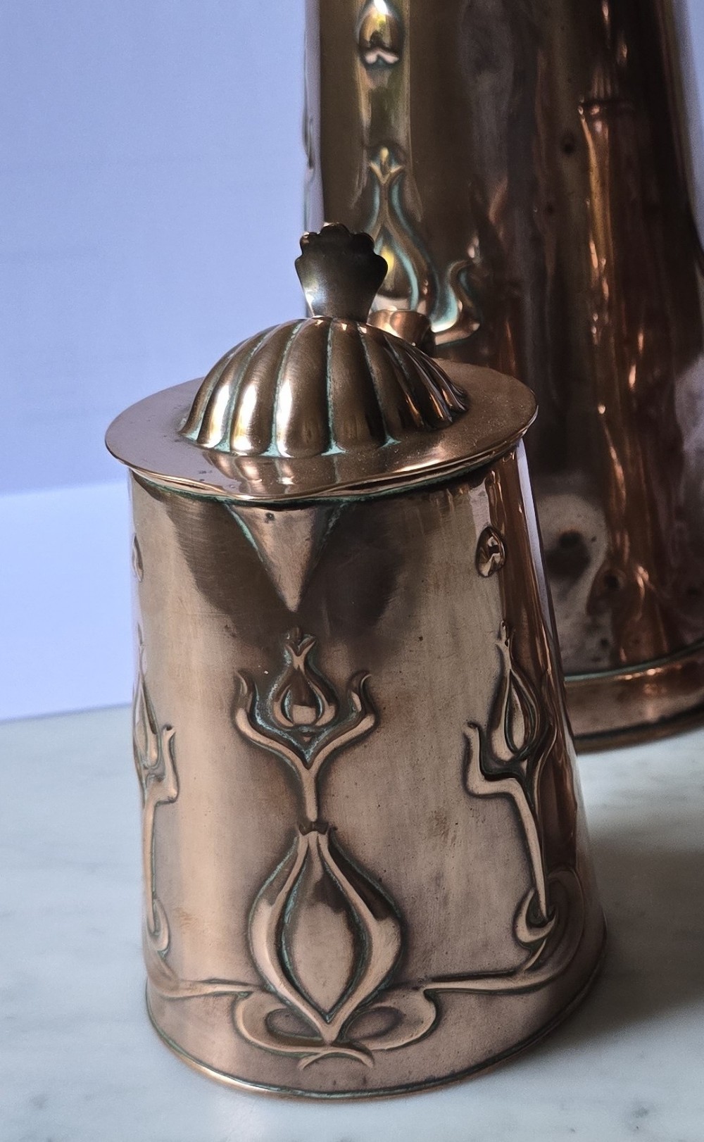 A set of three graduated copper jugs featuring embossed Art Nouveau floral motifs and shell-shaped hinged lids. View IV