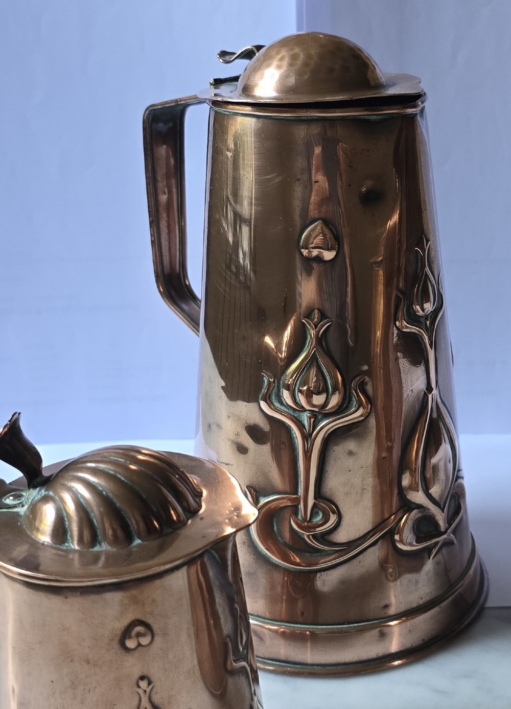 A set of three graduated copper jugs featuring embossed Art Nouveau floral motifs and shell-shaped hinged lids. View VIII