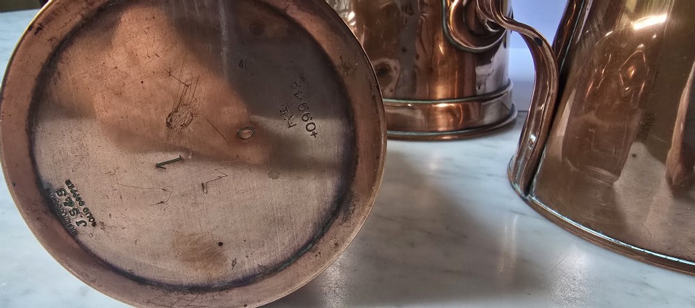A set of three graduated copper jugs featuring embossed Art Nouveau floral motifs and shell-shaped hinged lids. View X