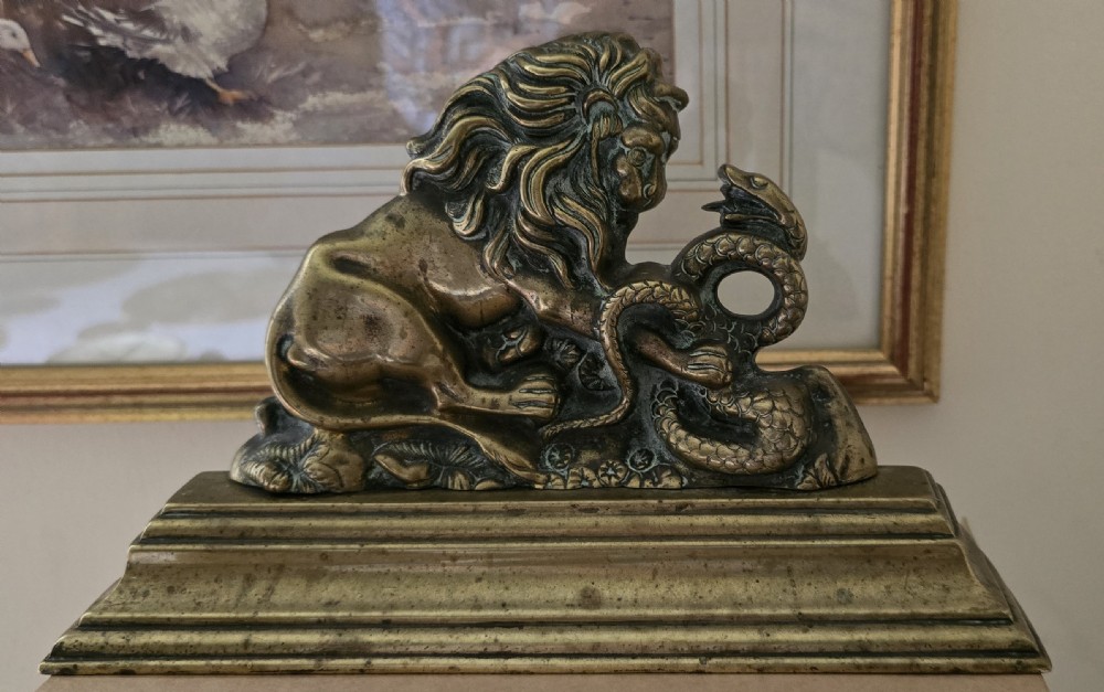A heavy cast brass Victorian doorstop featuring a sculptural lion wrestling a coiled serpent atop a moulded plinth base. View V