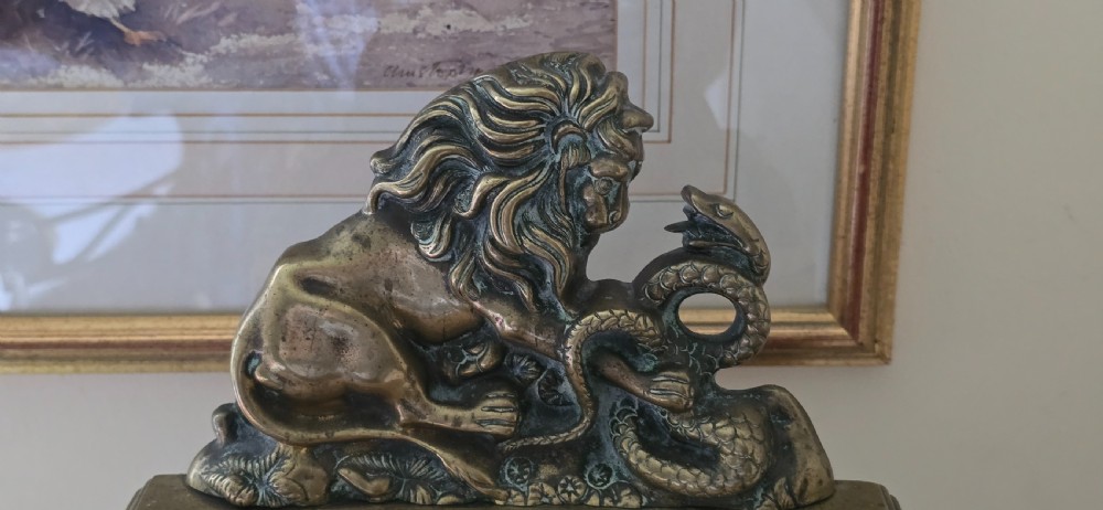 A heavy cast brass Victorian doorstop featuring a sculptural lion wrestling a coiled serpent atop a moulded plinth base. View VII
