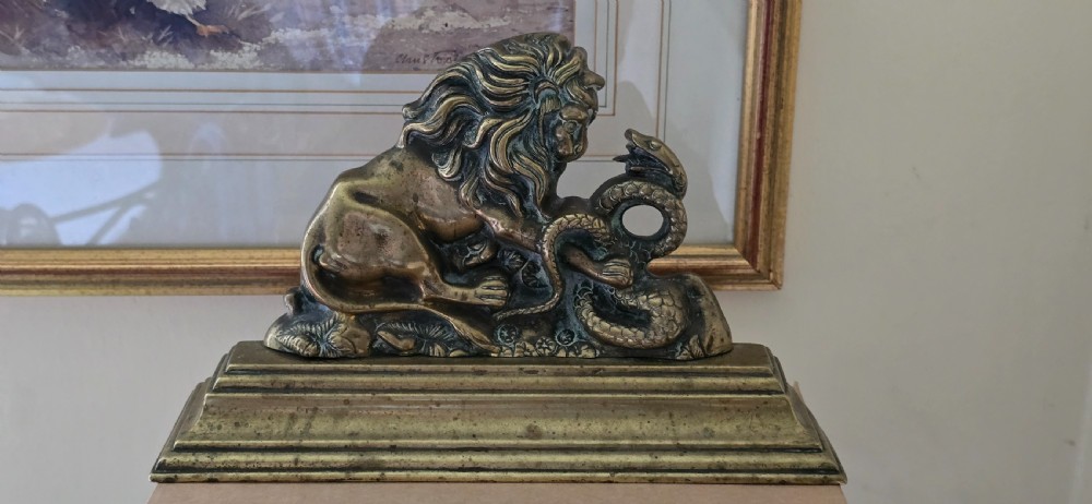 A heavy cast brass Victorian doorstop featuring a sculptural lion wrestling a coiled serpent atop a moulded plinth base. View VIII