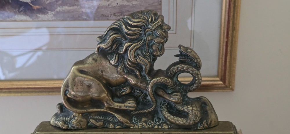 A heavy cast brass Victorian doorstop featuring a sculptural lion wrestling a coiled serpent atop a moulded plinth base. View X
