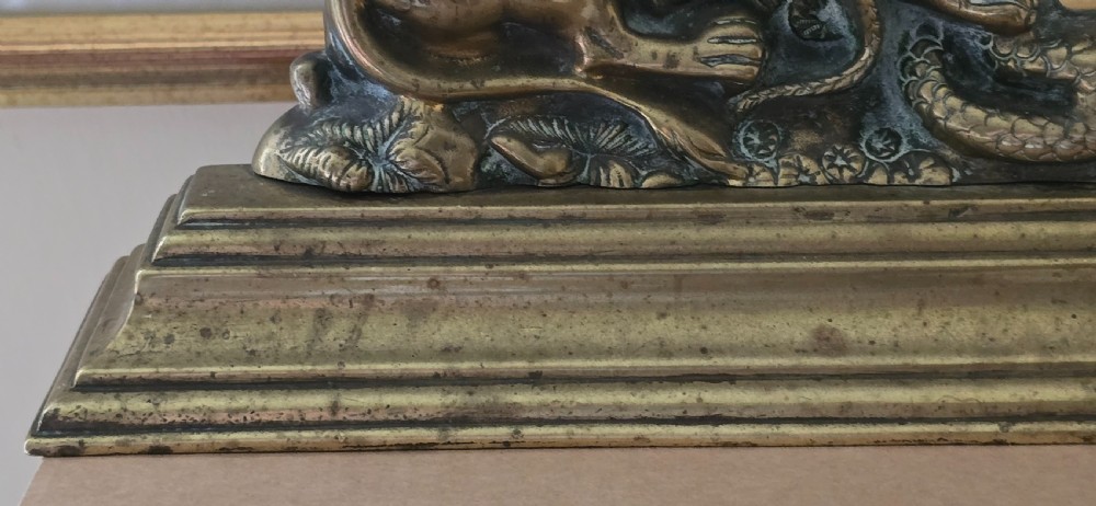 A heavy cast brass Victorian doorstop featuring a sculptural lion wrestling a coiled serpent atop a moulded plinth base. View XII