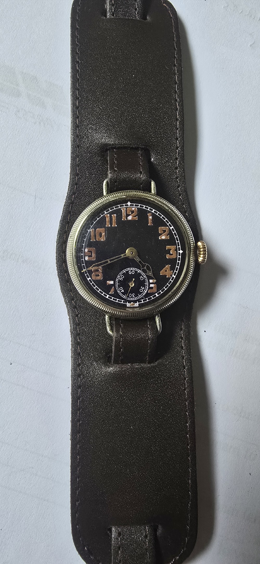 An antique military trench watch featuring a black dial with aged luminous numbers, cathedral hands, a small sub-seconds dial, wire lugs, and a coin-edge bezel. View III