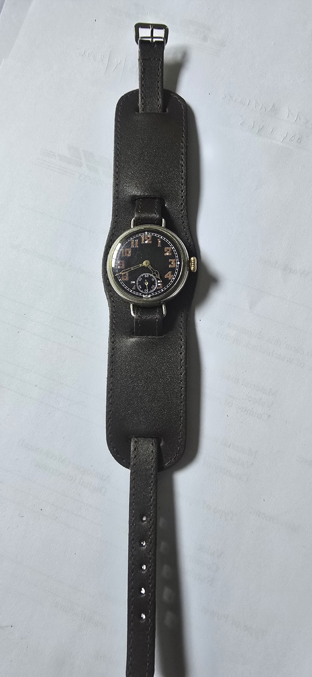 An antique military trench watch featuring a black dial with aged luminous numbers, cathedral hands, a small sub-seconds dial, wire lugs, and a coin-edge bezel. View IV