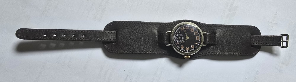 An antique military trench watch featuring a black dial with aged luminous numbers, cathedral hands, a small sub-seconds dial, wire lugs, and a coin-edge bezel. View V