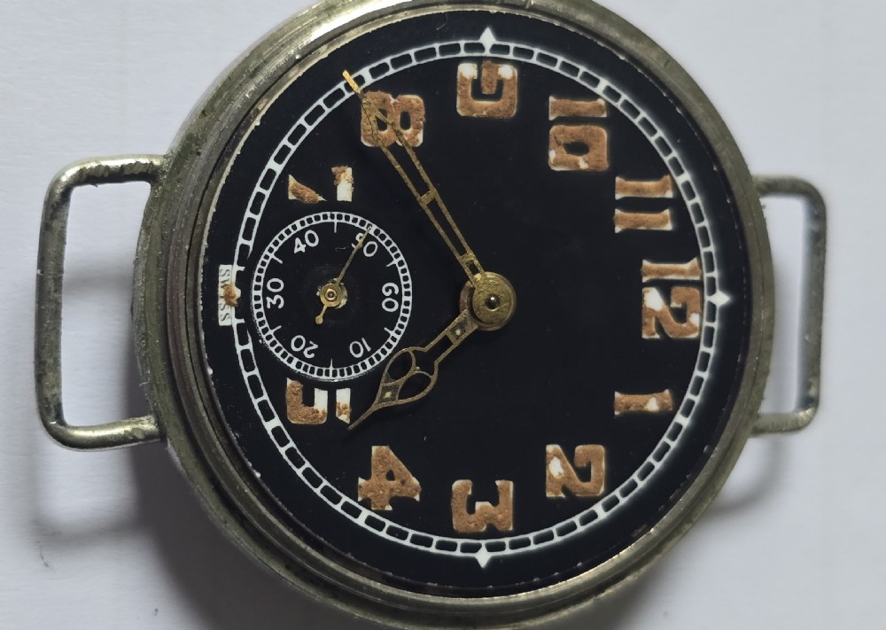 An antique military trench watch featuring a black dial with aged luminous numbers, cathedral hands, a small sub-seconds dial, wire lugs, and a coin-edge bezel. View IX
